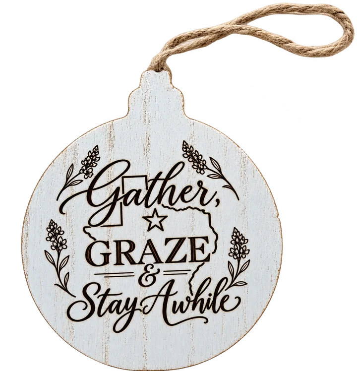White wood ornament engraved with Gather, Graze and Stay Awhile, Texas outline and bluebonnets, hung on jute twine